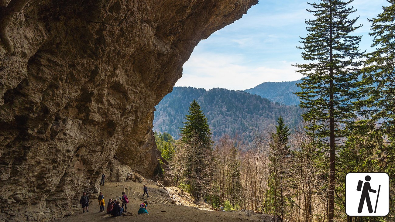A cave like overhang over a trail with a mountain view.