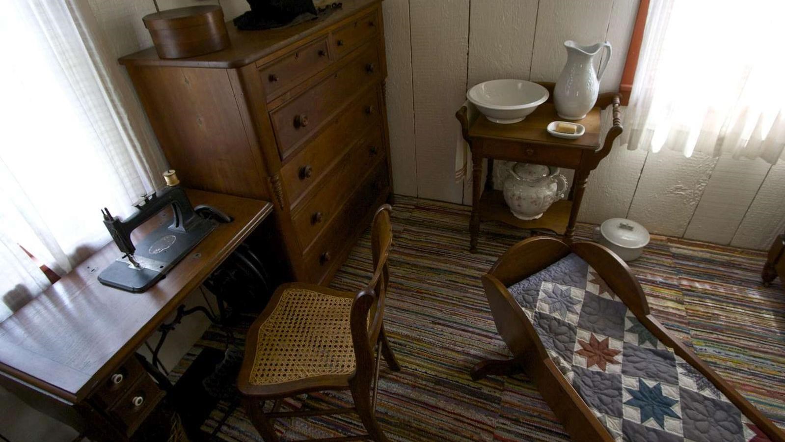 A bedroom appears cramped with a cradle, dresser, sewing machine, and a night stand.