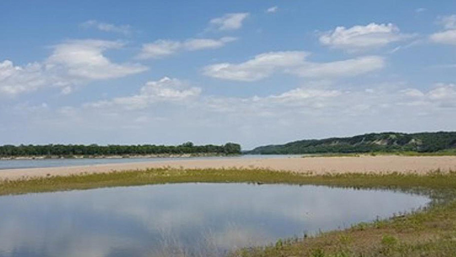Bow Creek river access with sandbar and and water in the left side of the image. Grass along water. 