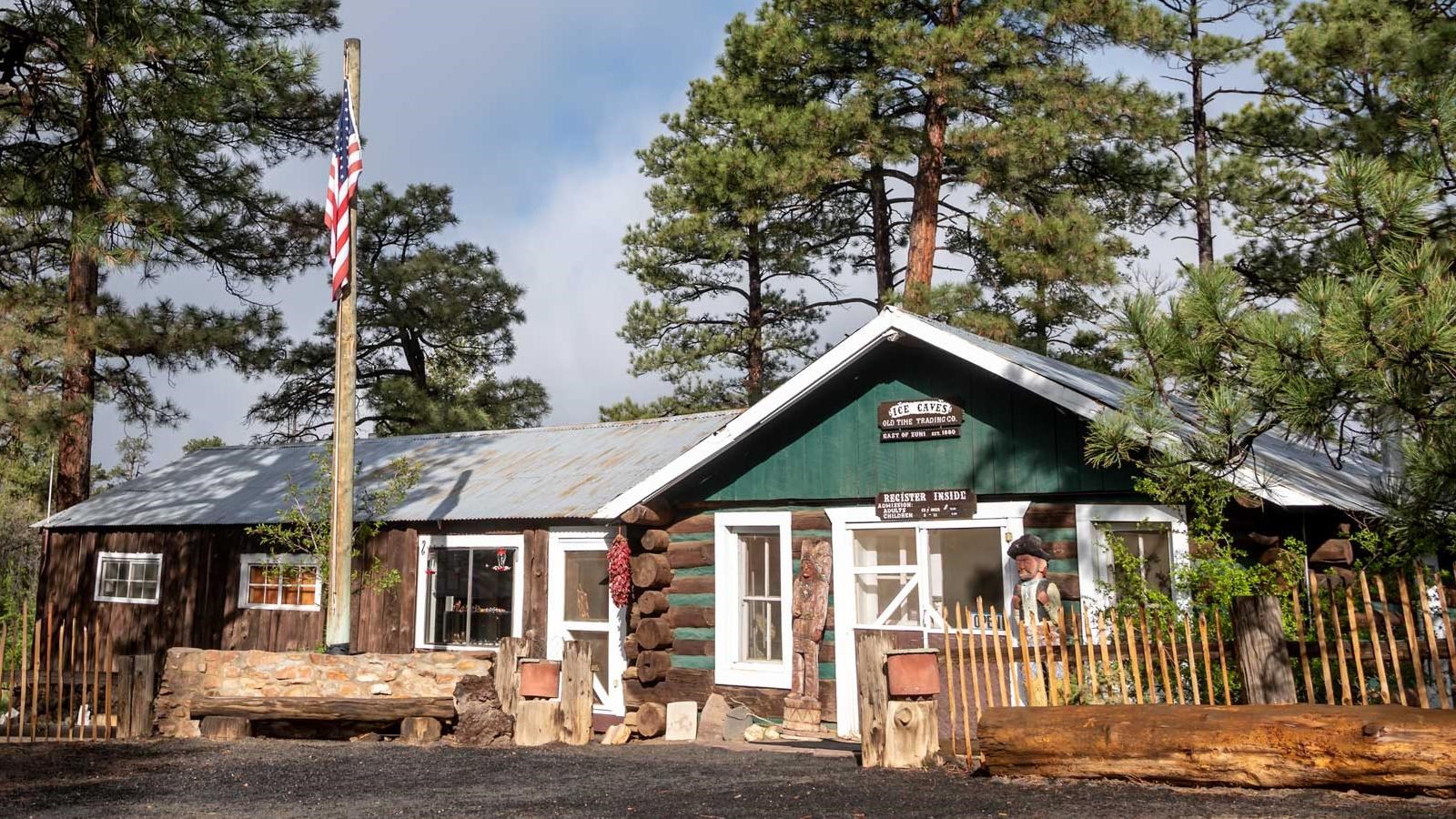 A green and white building sits between large pine trees and assorted decorations.