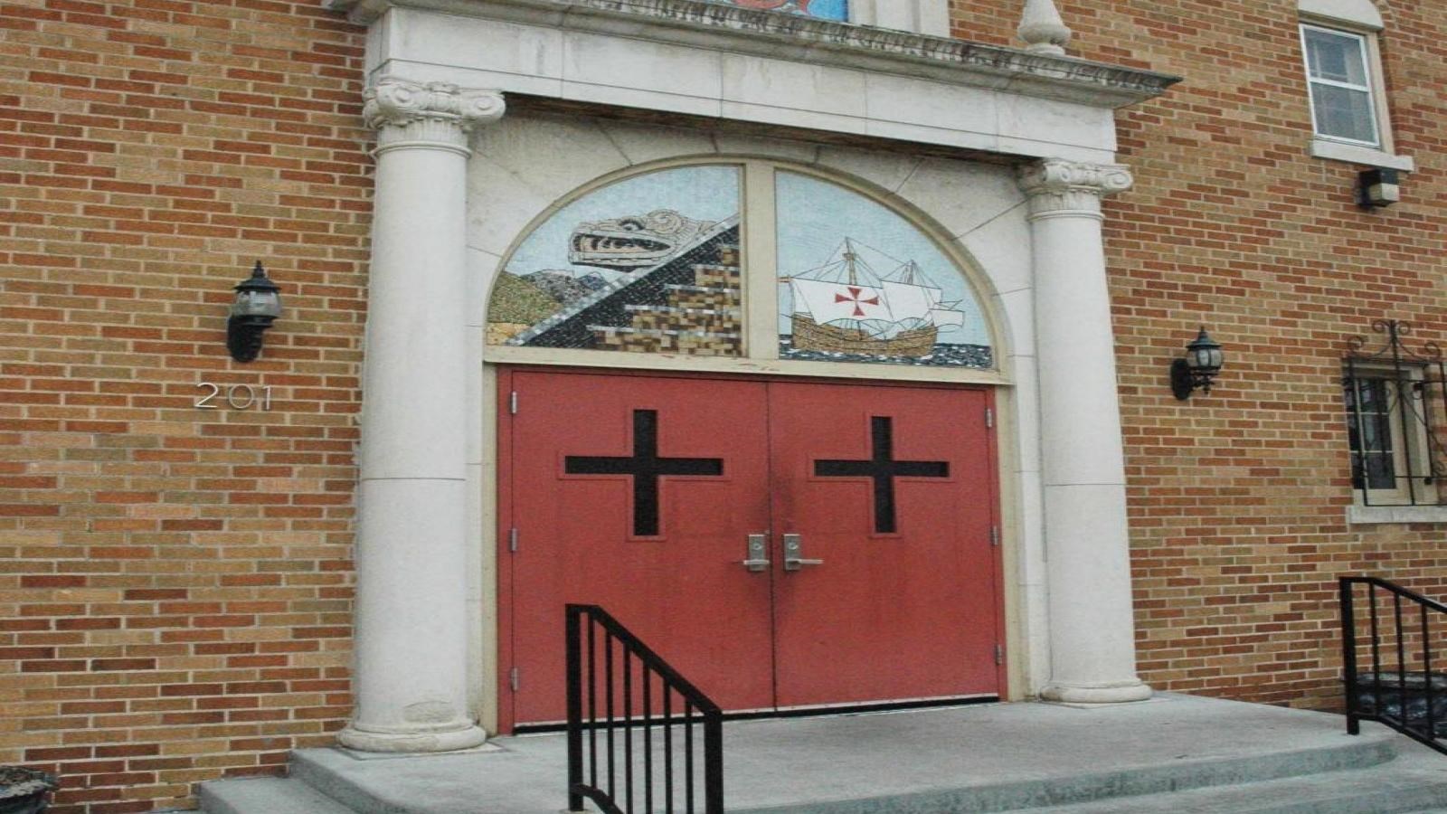 A flight of three steps lead to red double doors with a cross design on the front of the doors.