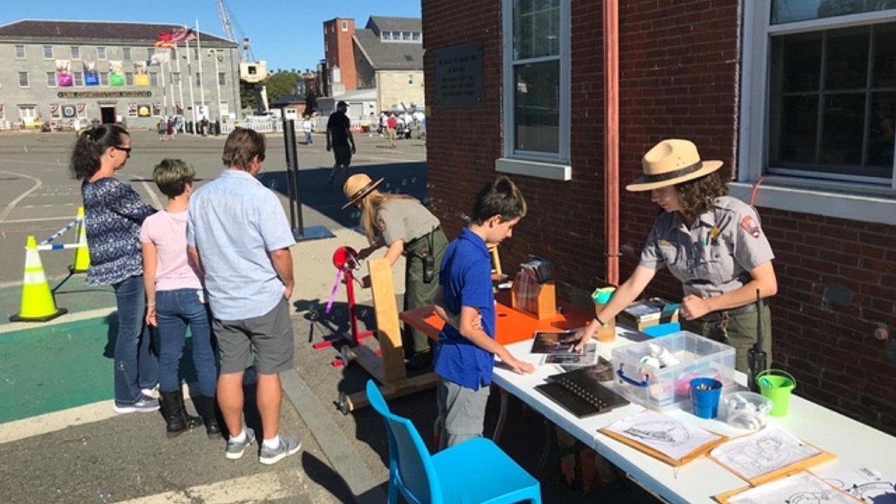 Ranger standing behind a table facing a child working on an activity. Other activities behind them.