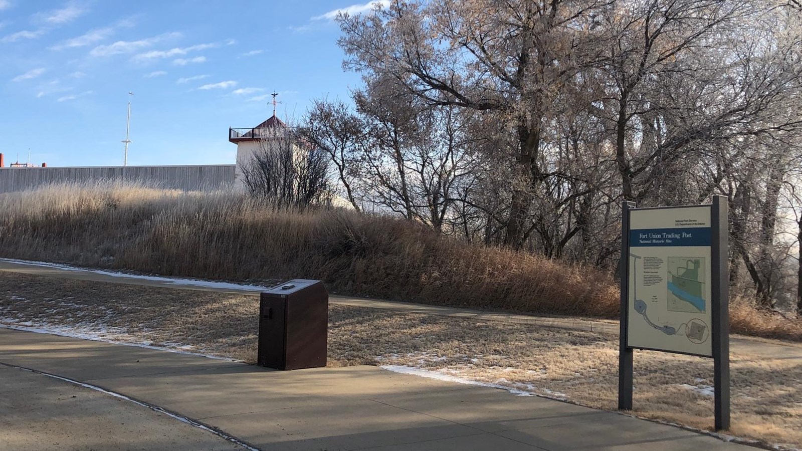 Exhibit at base of grassy hill, with trees and Fort wall and Bastion at crest of hill.