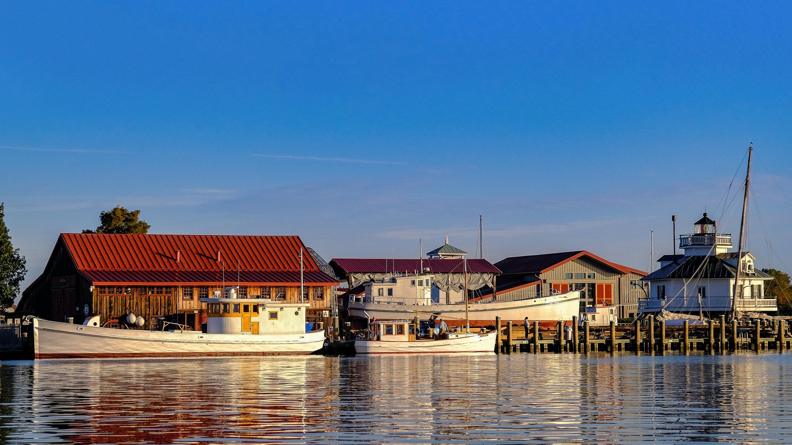 Boats docked at the Chesapeake Bay Maritime Museum with buildings and lighthouse in the background.
