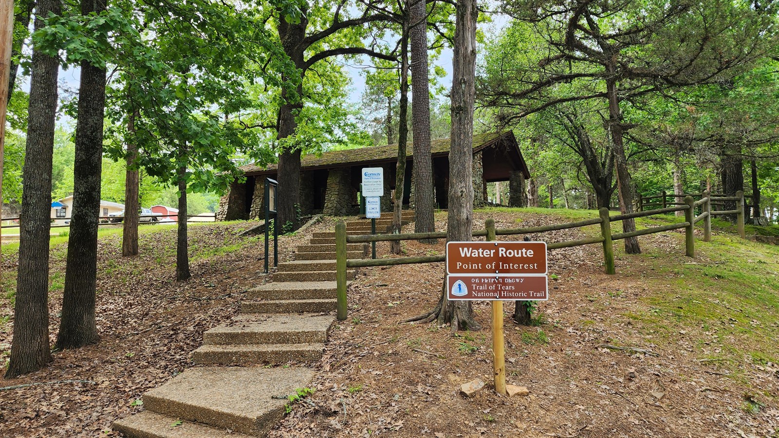 A stone staircase leads up to an old wooden, one story log cabin, in a forested setting.