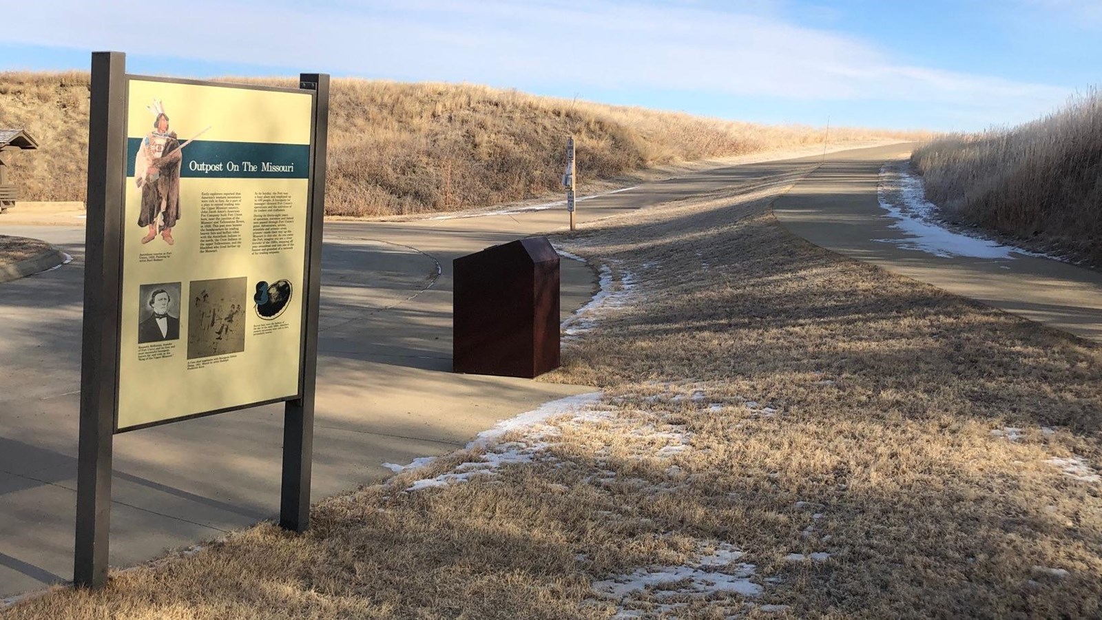 Exhibit stands on cement walkway winding up hill, hill is grassy.
