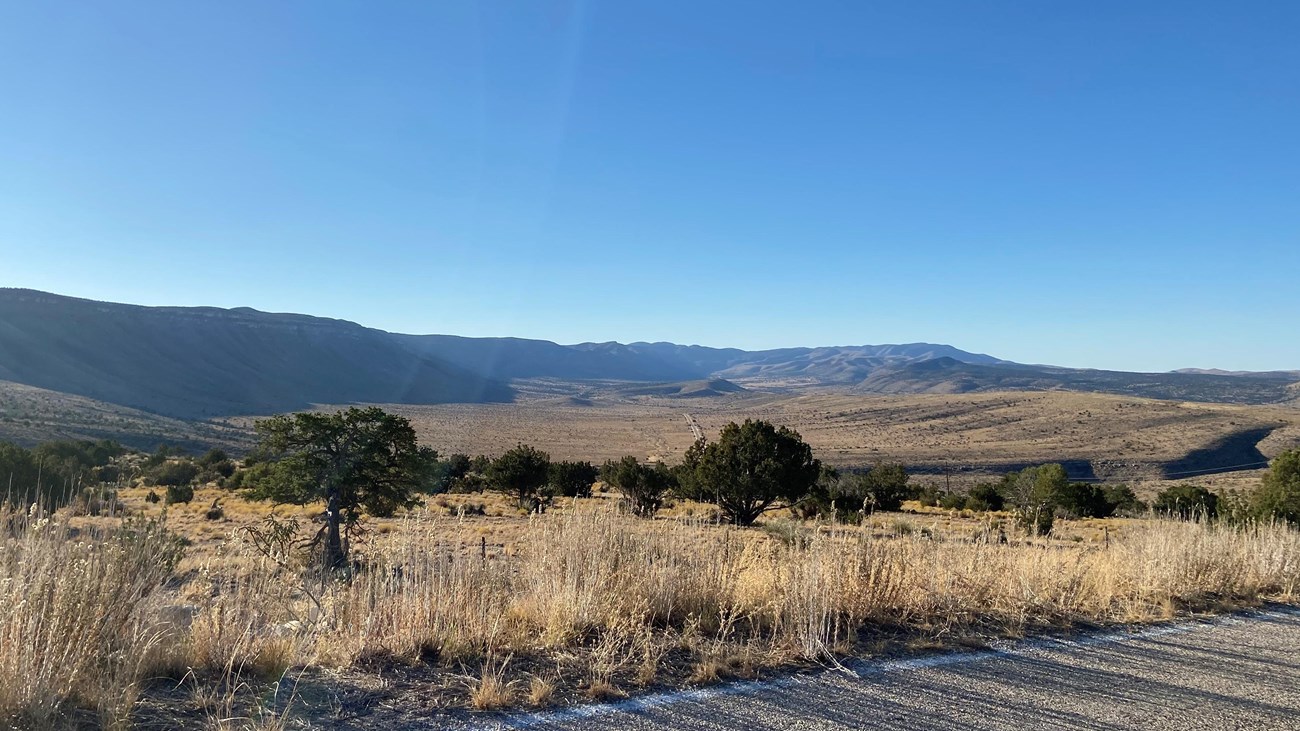 View from a road of a long canyon wall in the desert landscape.