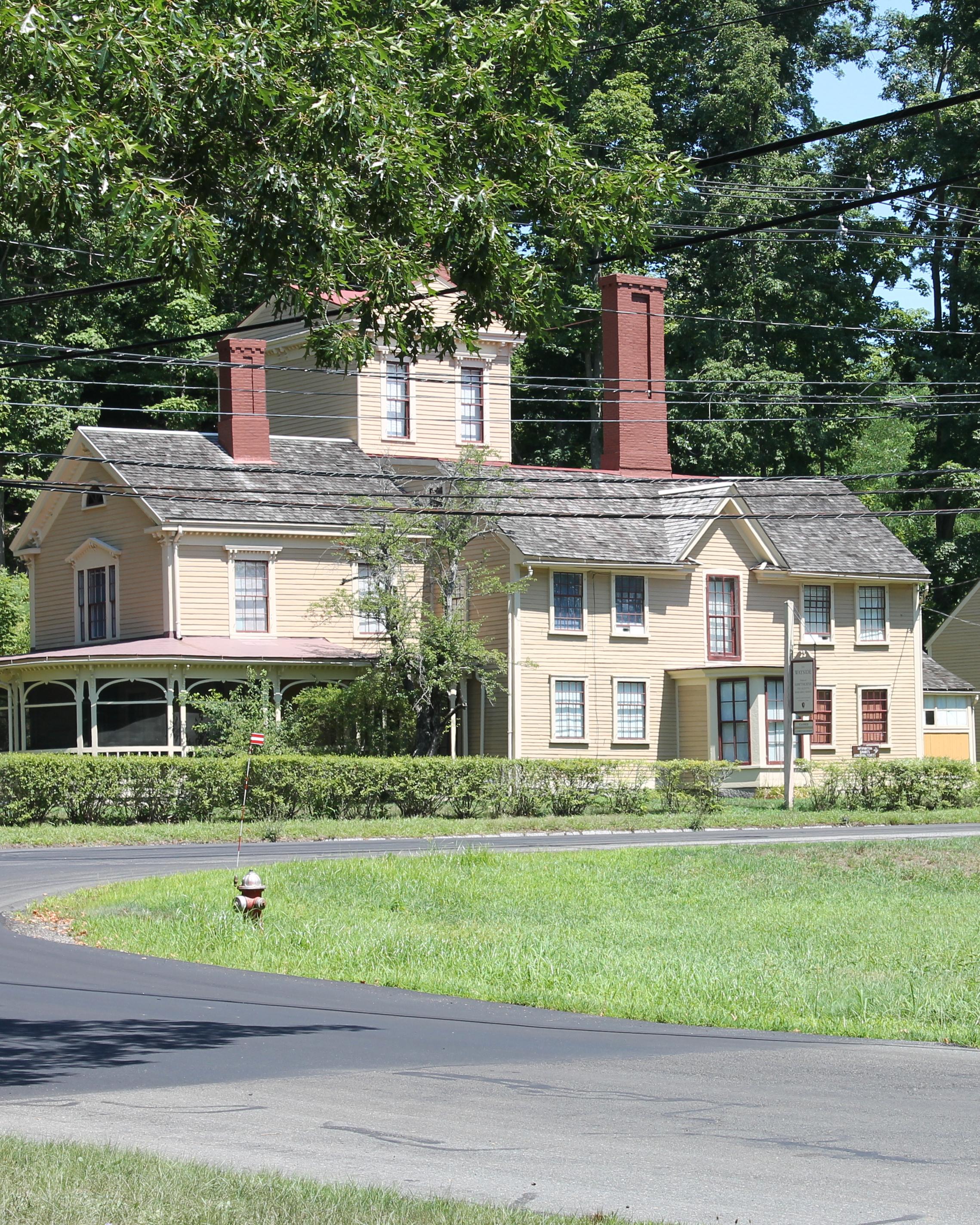 A wooden house surrounded by leafy trees. The house has many additions including a central tower.