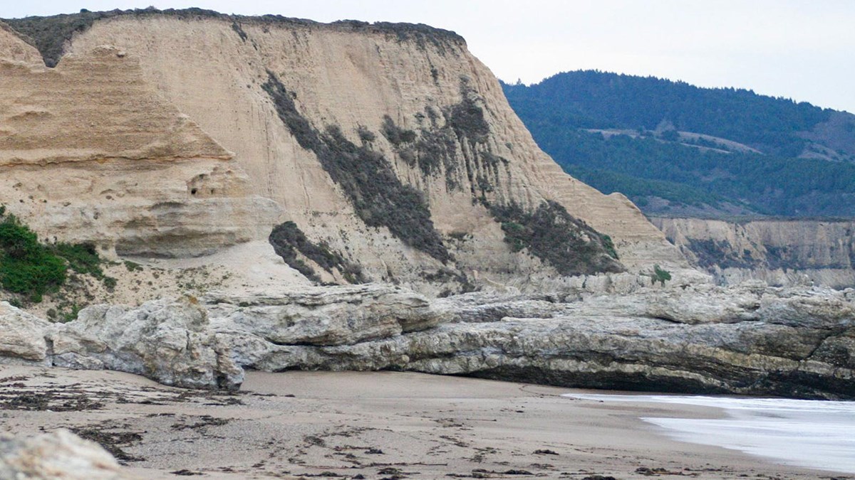 On the left, eroded bluffs rise above rock outcrops that stretch into a bay on the right.