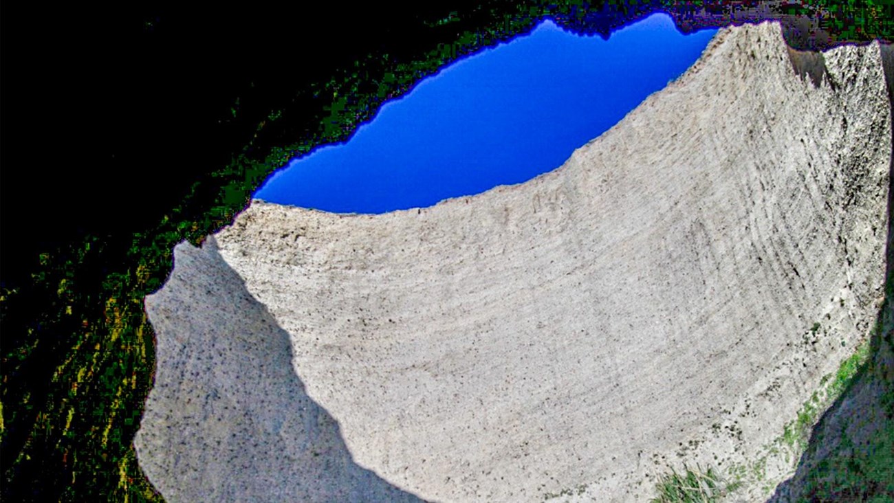 Looking up at blue sky visible through a large circular hole in the roof of a sea cave.