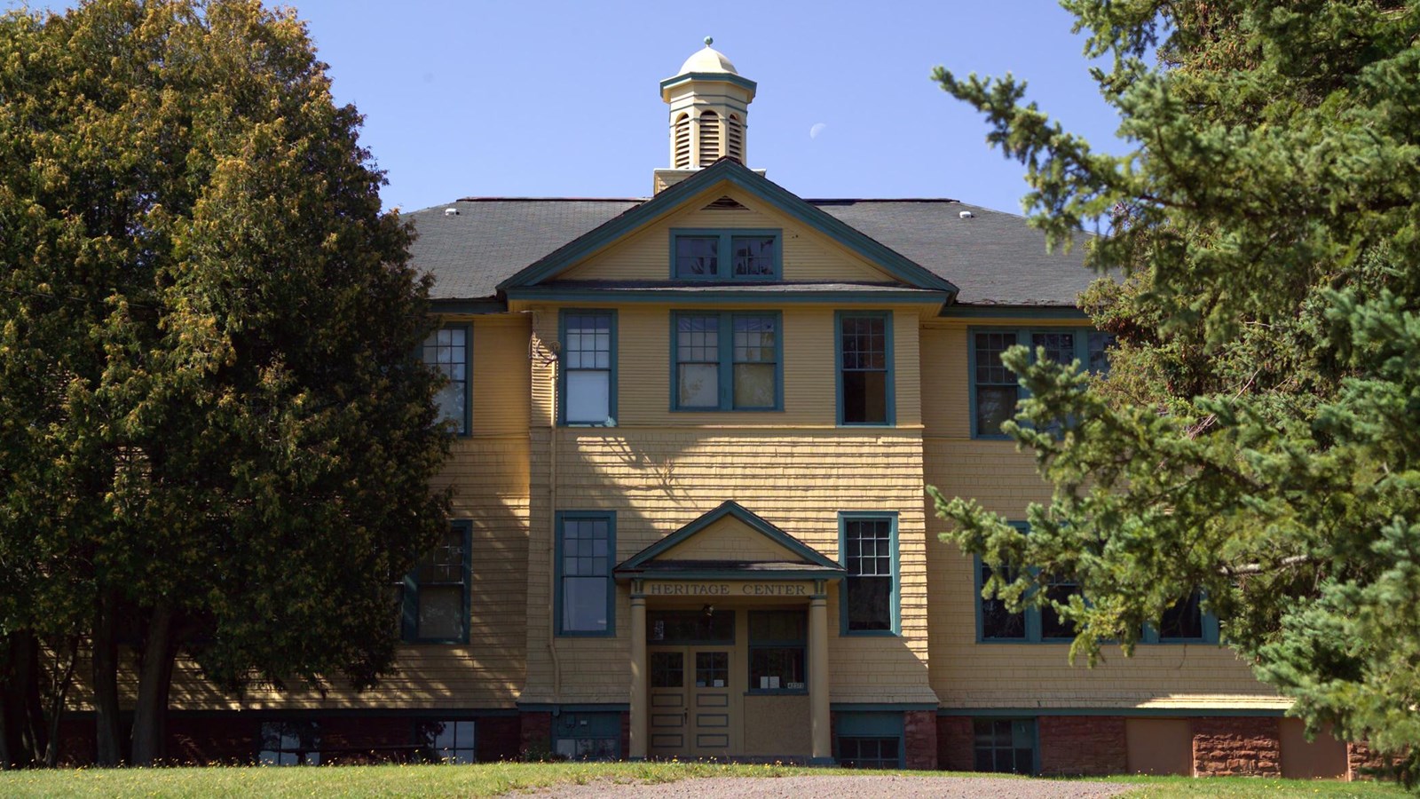 Summer scene of yellow three-story wooden building with red sandstone foundation.
