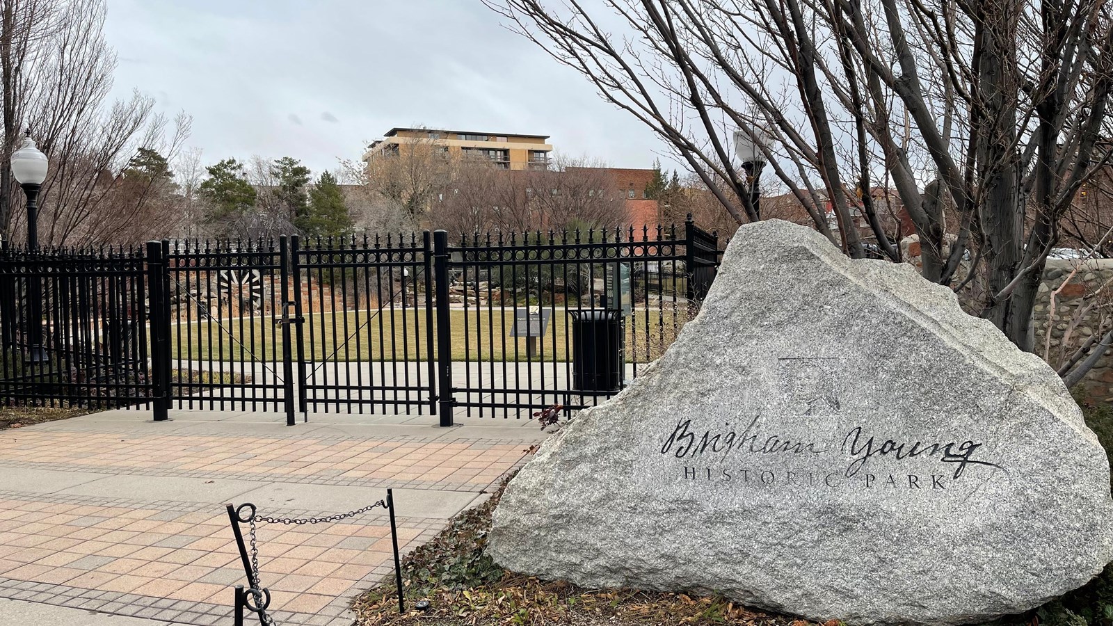 A large stone entry sign sits in front of a black metal fence surrounding a park.
