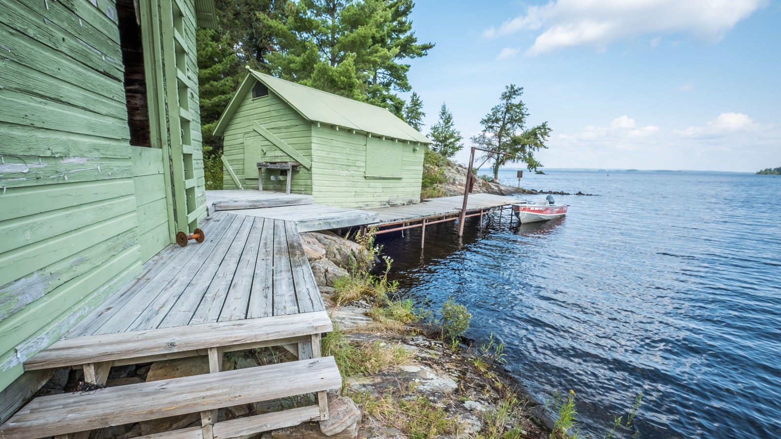 Two old wooden buildings painted a light green along a shoreline connected to a dock.