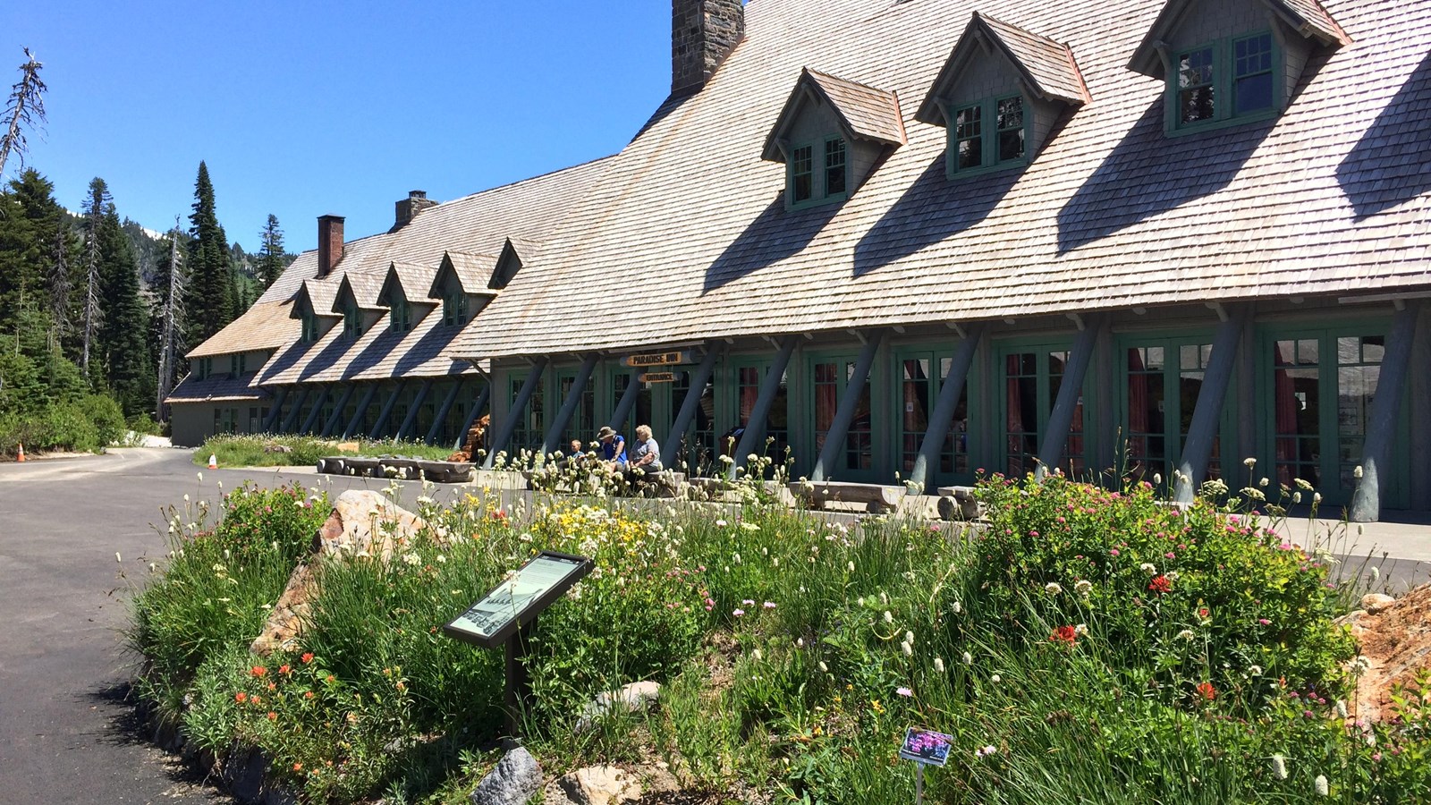 A small vertical panel in an island of wildflowers in a parking area in front of a building.