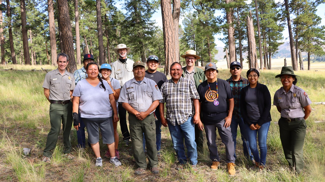 A group of park rangers and Pueblo of Jemez leaders stand together in an old growth forest.