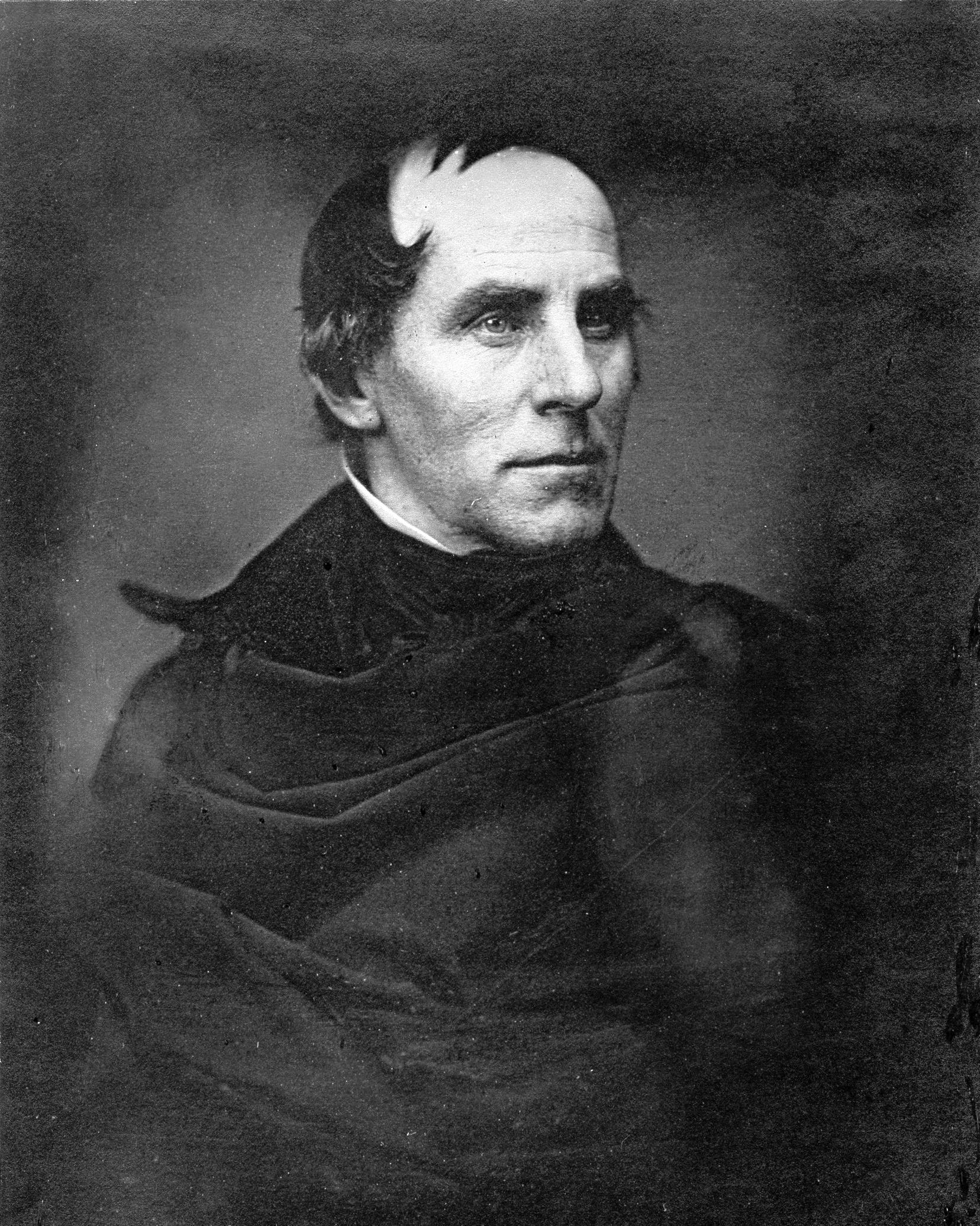 A photographic portrait of a man with hair sweeping forward and dressed in black.