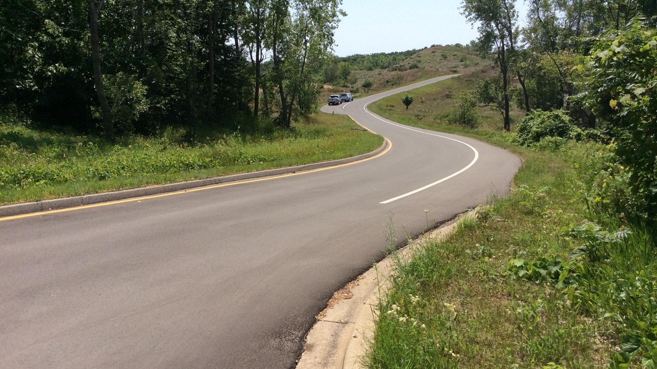 A paved road winds through plant covered sand dunes.
