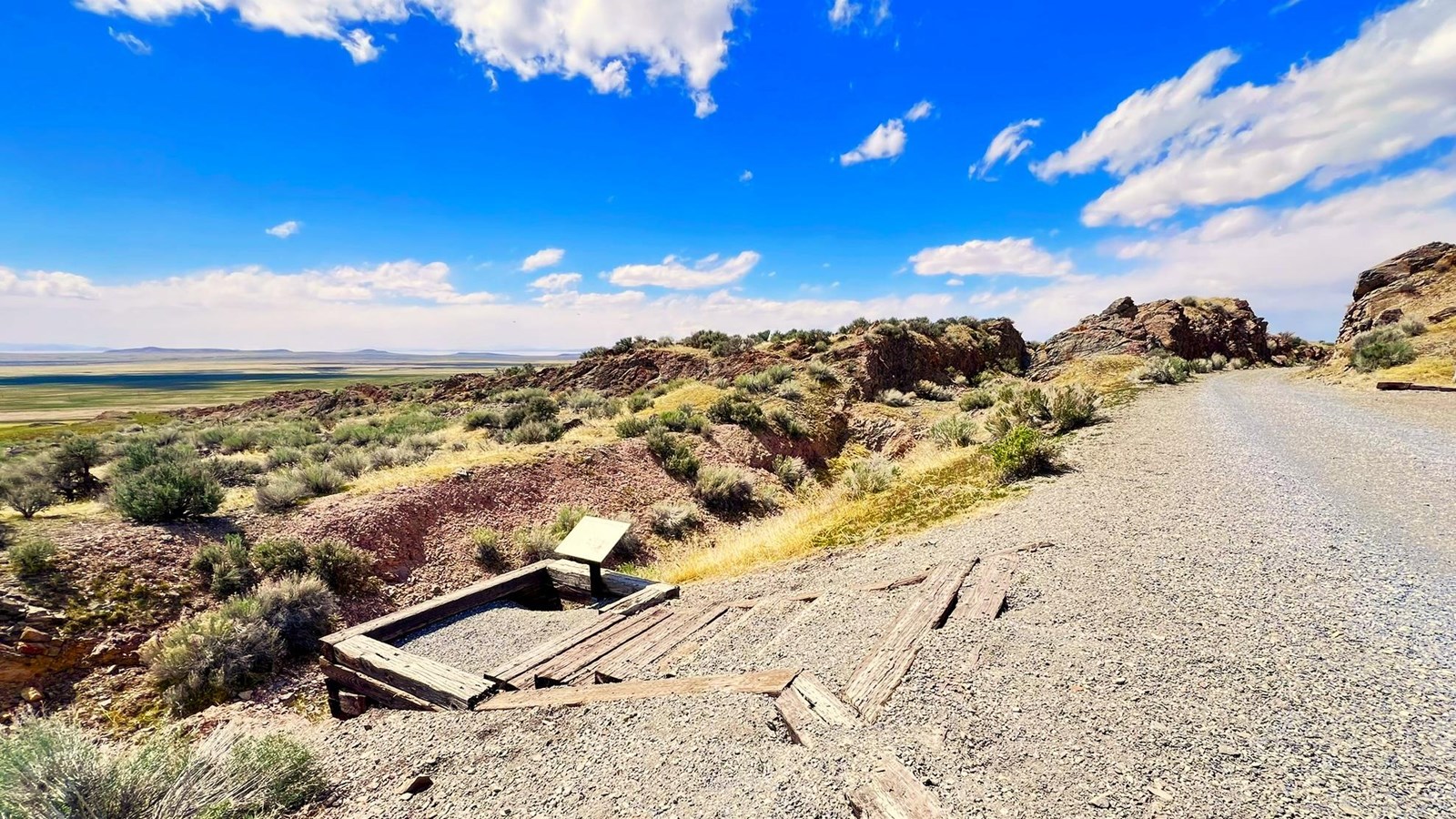 Gravel road through green, yellow and brown sagebrush landscapes. Cut rock hils