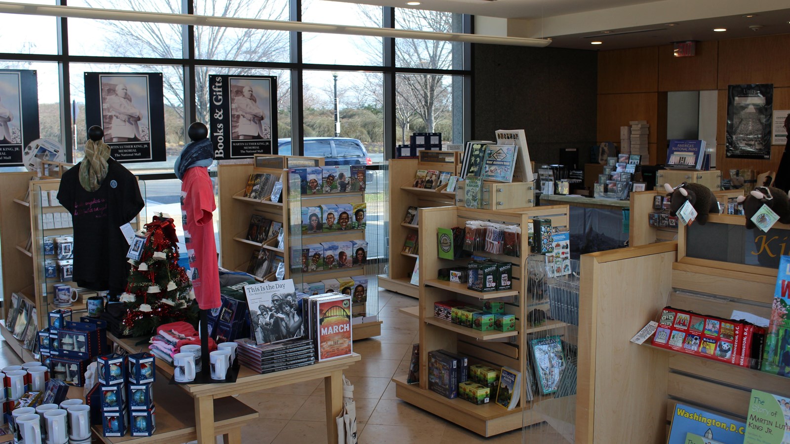 Books and other souvenirs line shelves in a room with tall glass windows.