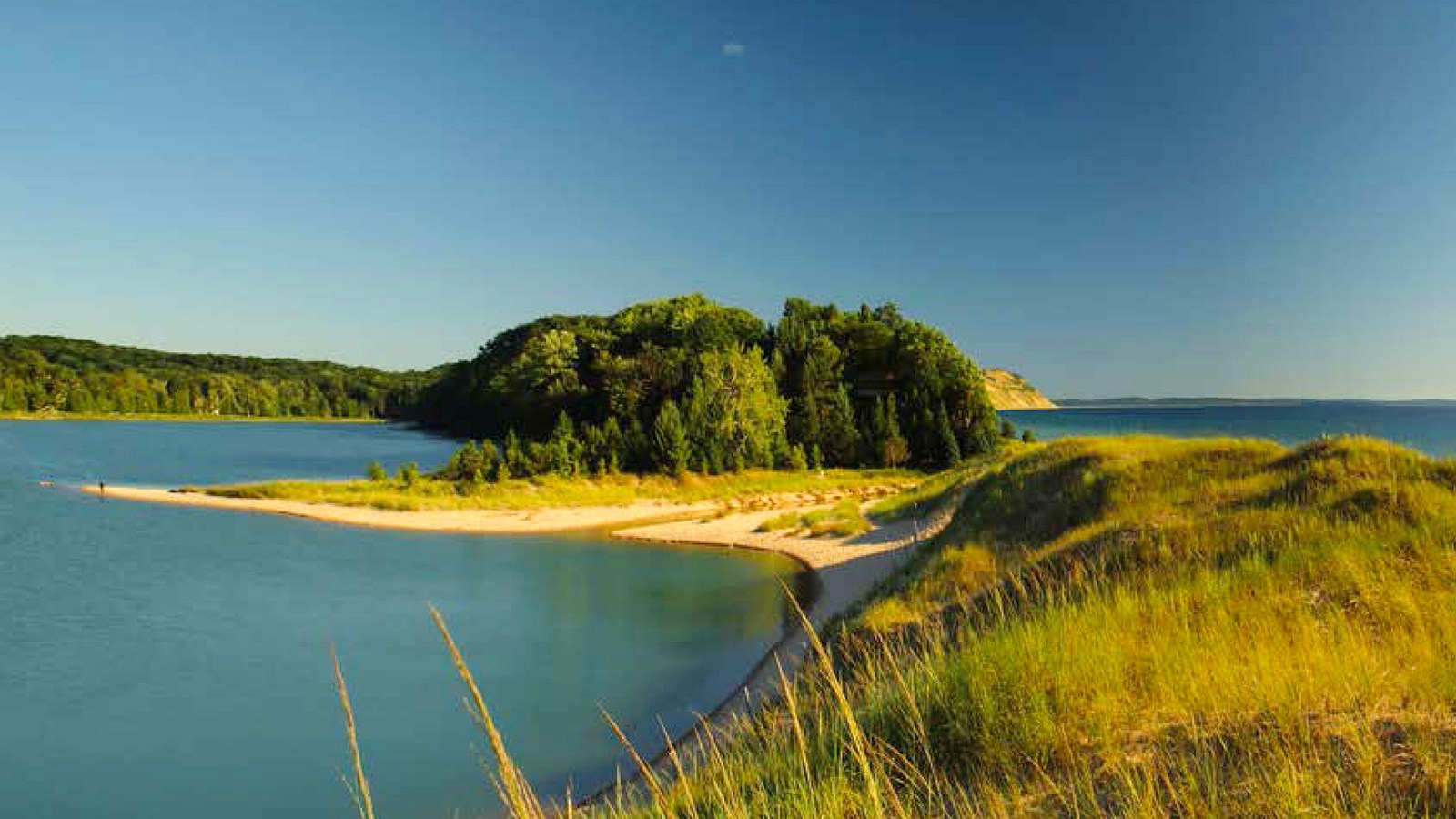 A sand ridge covered with green beach grass separates an inland lake from a large lake