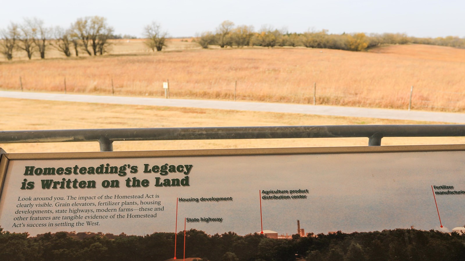 Informational sign stands in front of restored tallgrass prairie and an Osage orange hedgerow.