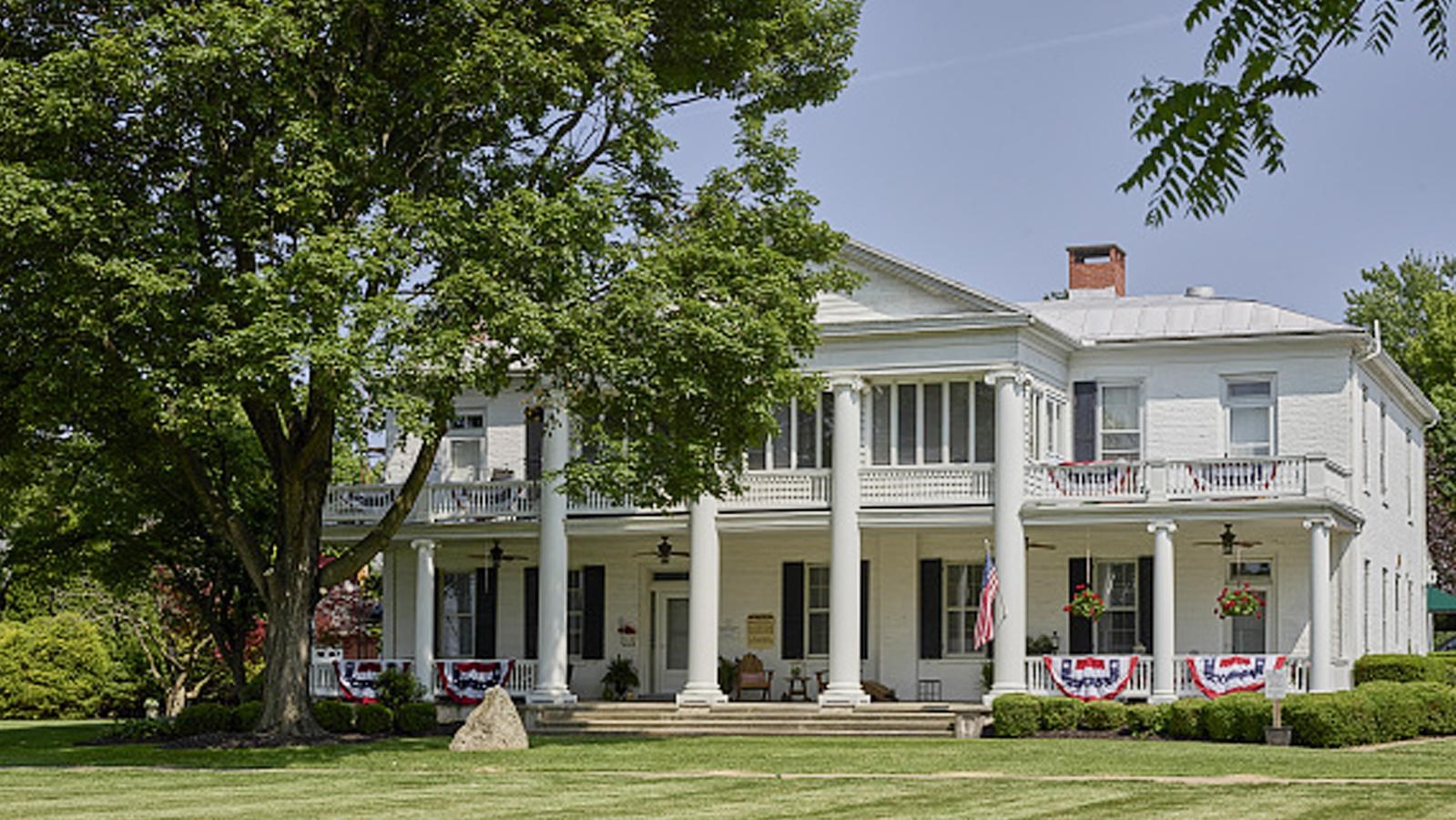 A white two-story house with columns with a well manicured green lawn.