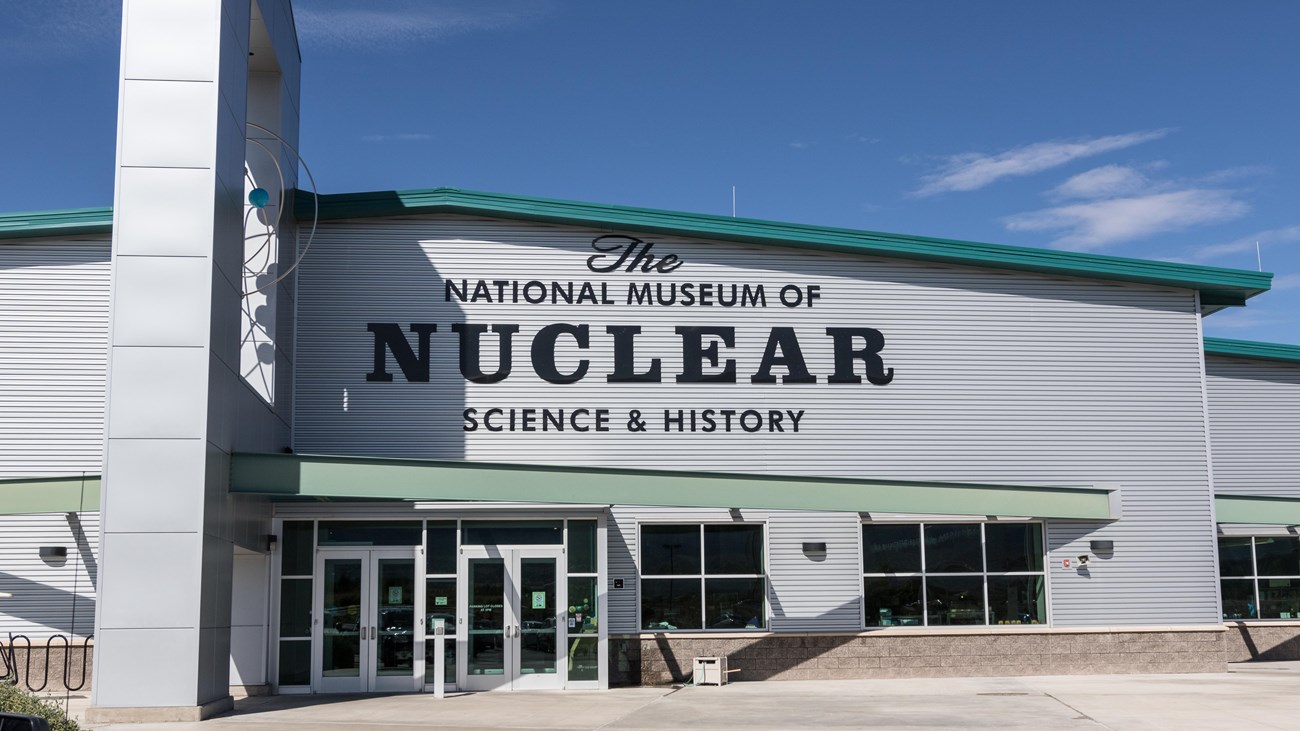 A light grey building, with a sign, with text that says National Museum of Nuclear Science & History