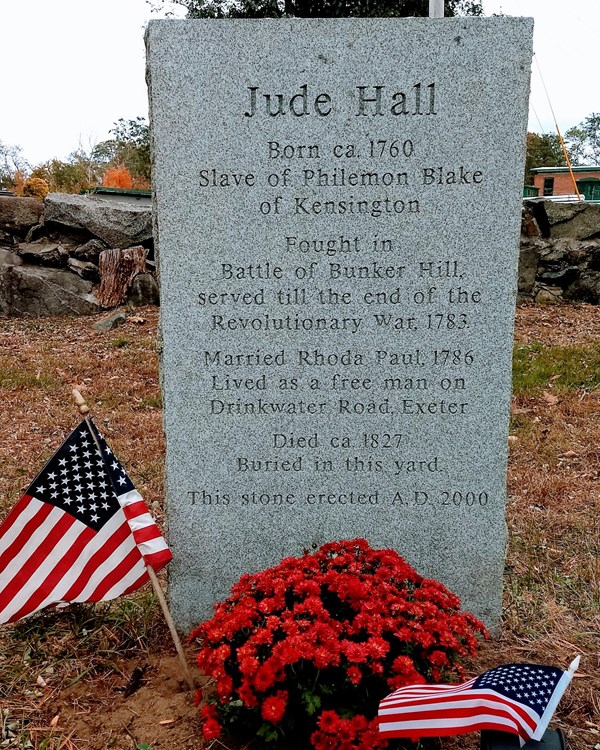 Grave stone of Jude Hall in the fall with a flag and flowers in front of it.