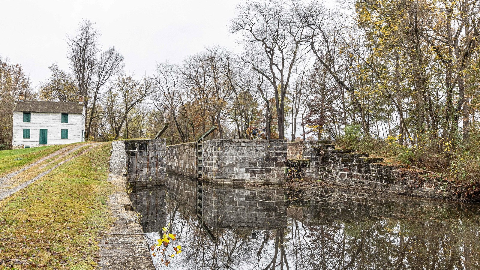 A tall water filled lock sits on the right with the towpath and lockhouse on the left. 