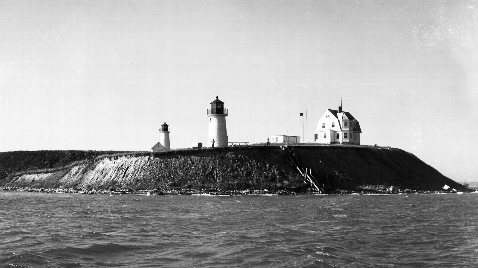 View from the ocean of two twin white lighthouses near a large white house on an island. 