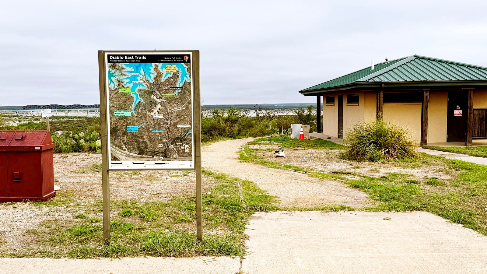 Trailhead sign next to trail and comfort station or restroom.