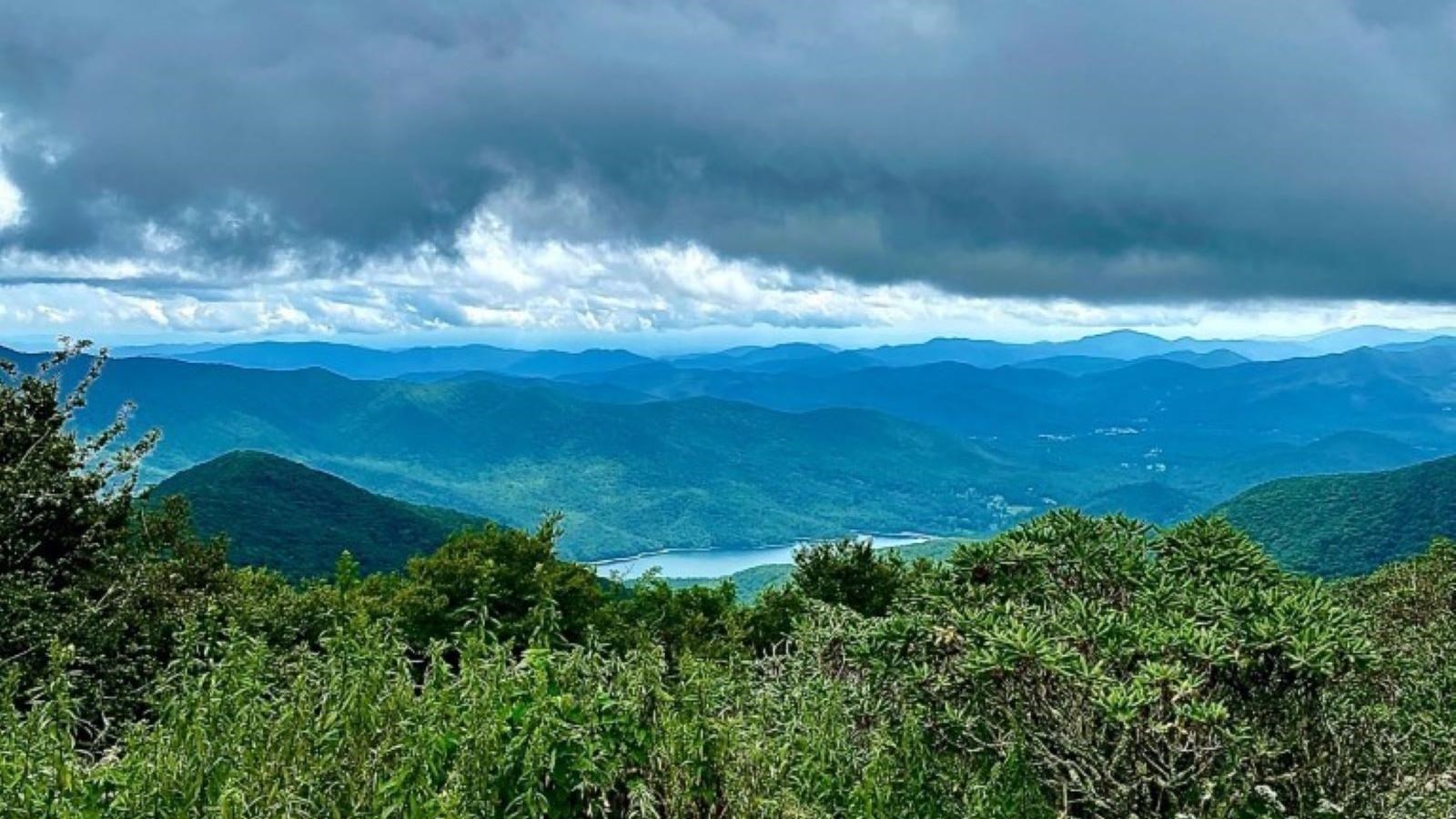View of layered mountains and heavy clouds with body of water in distance