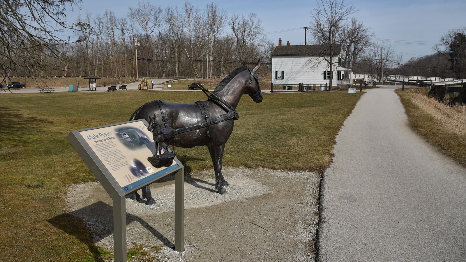 Life-sized mule statue and exhibit with tactile bronze mule; paved trail leads to a white building.