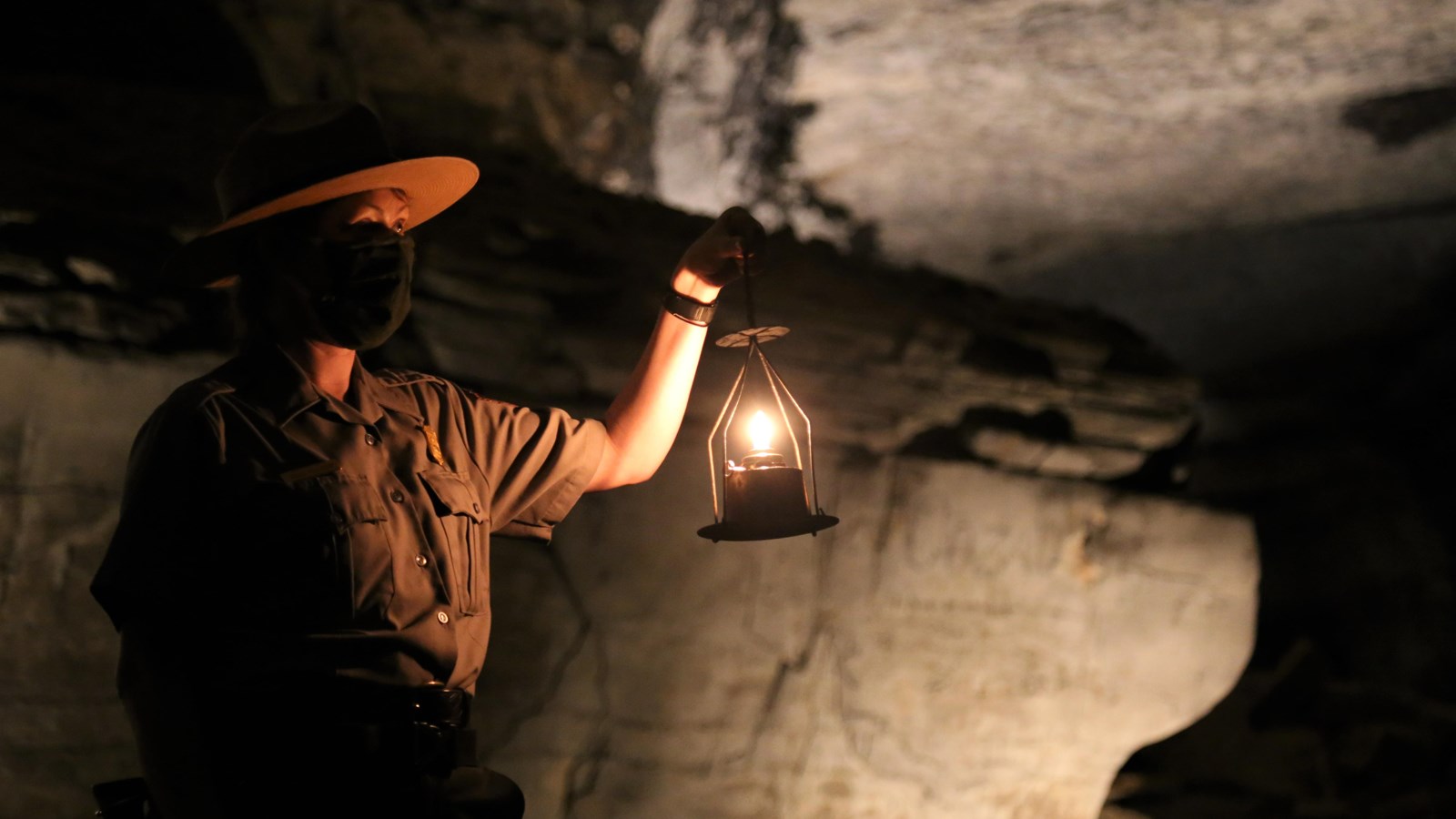 A park ranger standing in a dark cave holding a lantern.