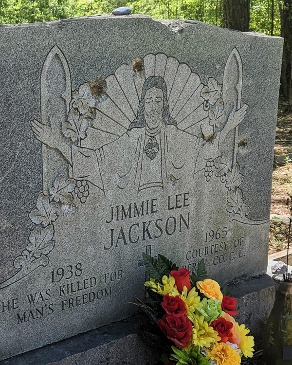 A large gravestone with an angel etched on the stone. Colorful flowers rest at the bottom.