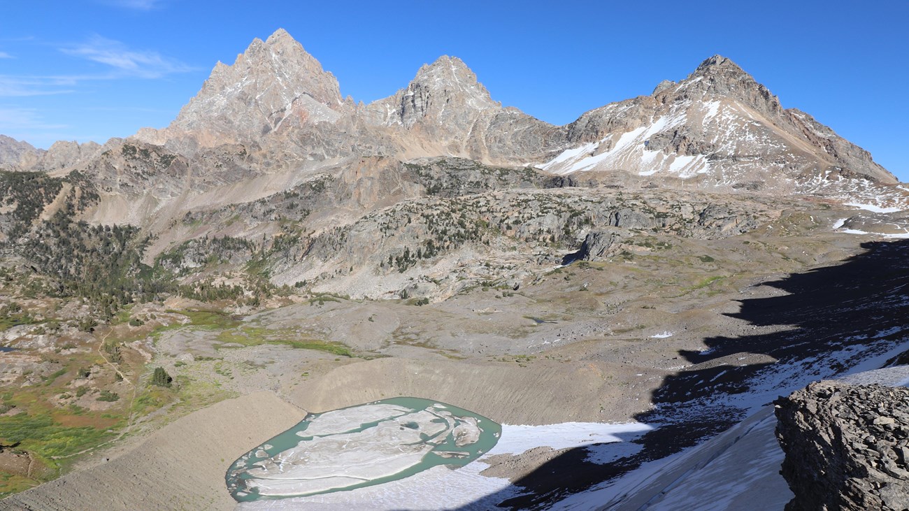 3 mountain peaks stand tall above a glacially carved valley, a glacial lake, and a small glacier. 