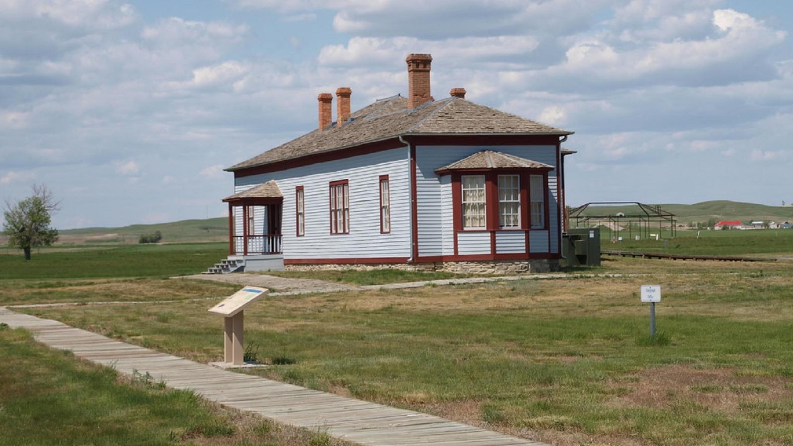 A paneled boardwalk leads to an historic, light blue building with red trim.