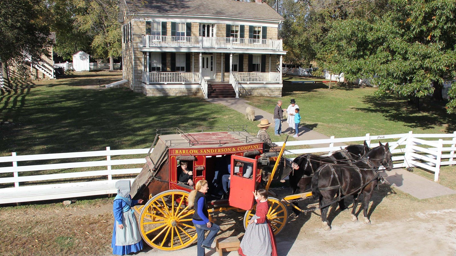 A stagecoach with horses stands in front of a historic home.