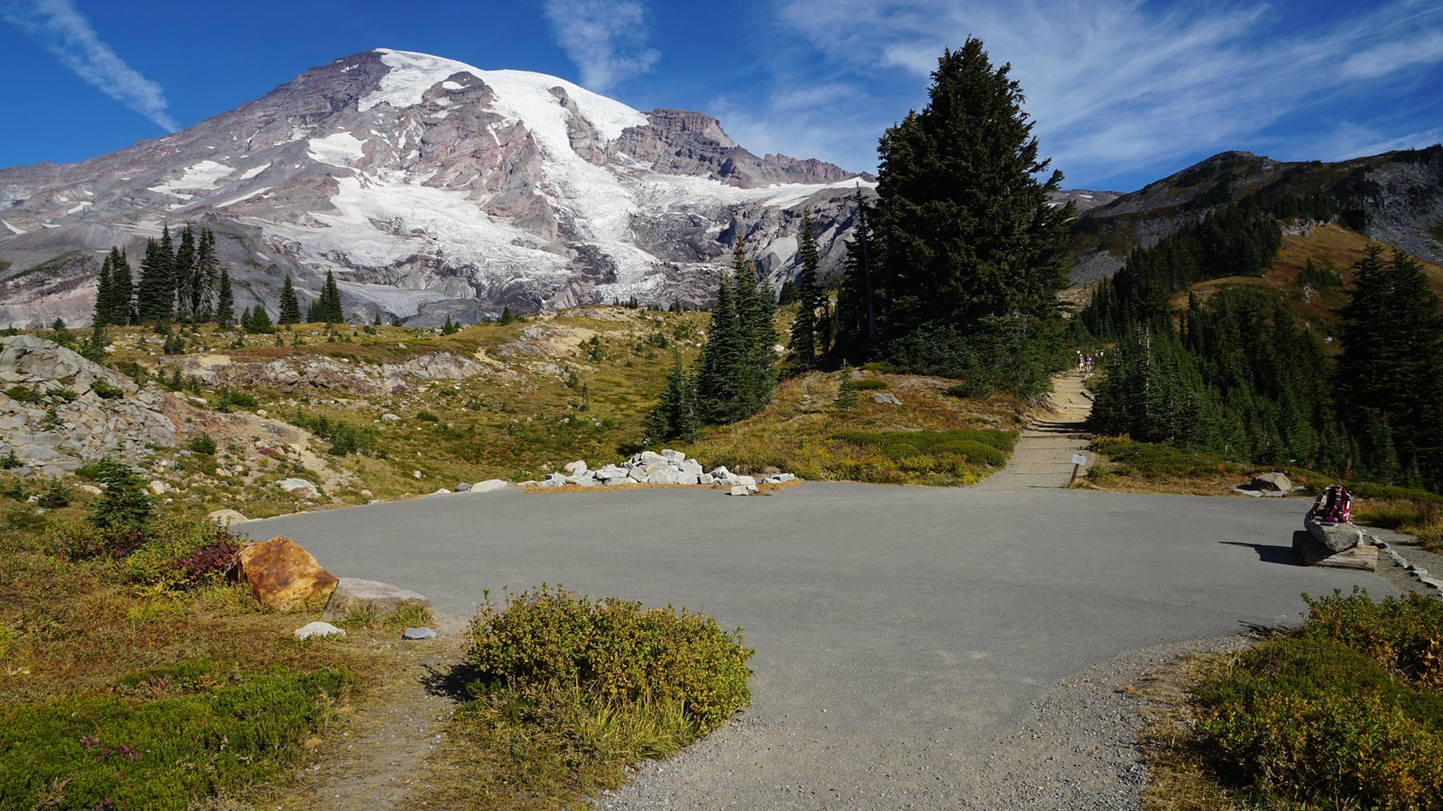 A large, paved area with several trails branching from it with views of Mount Rainier. 
