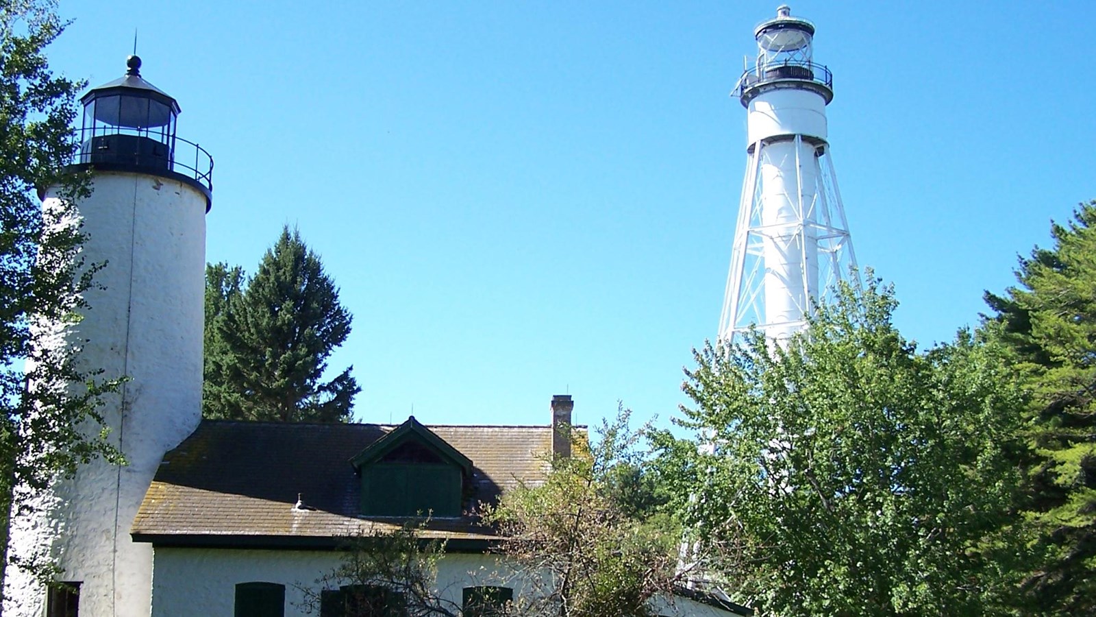 A group of people standing on a lawn with two white lighthouses in the background. 