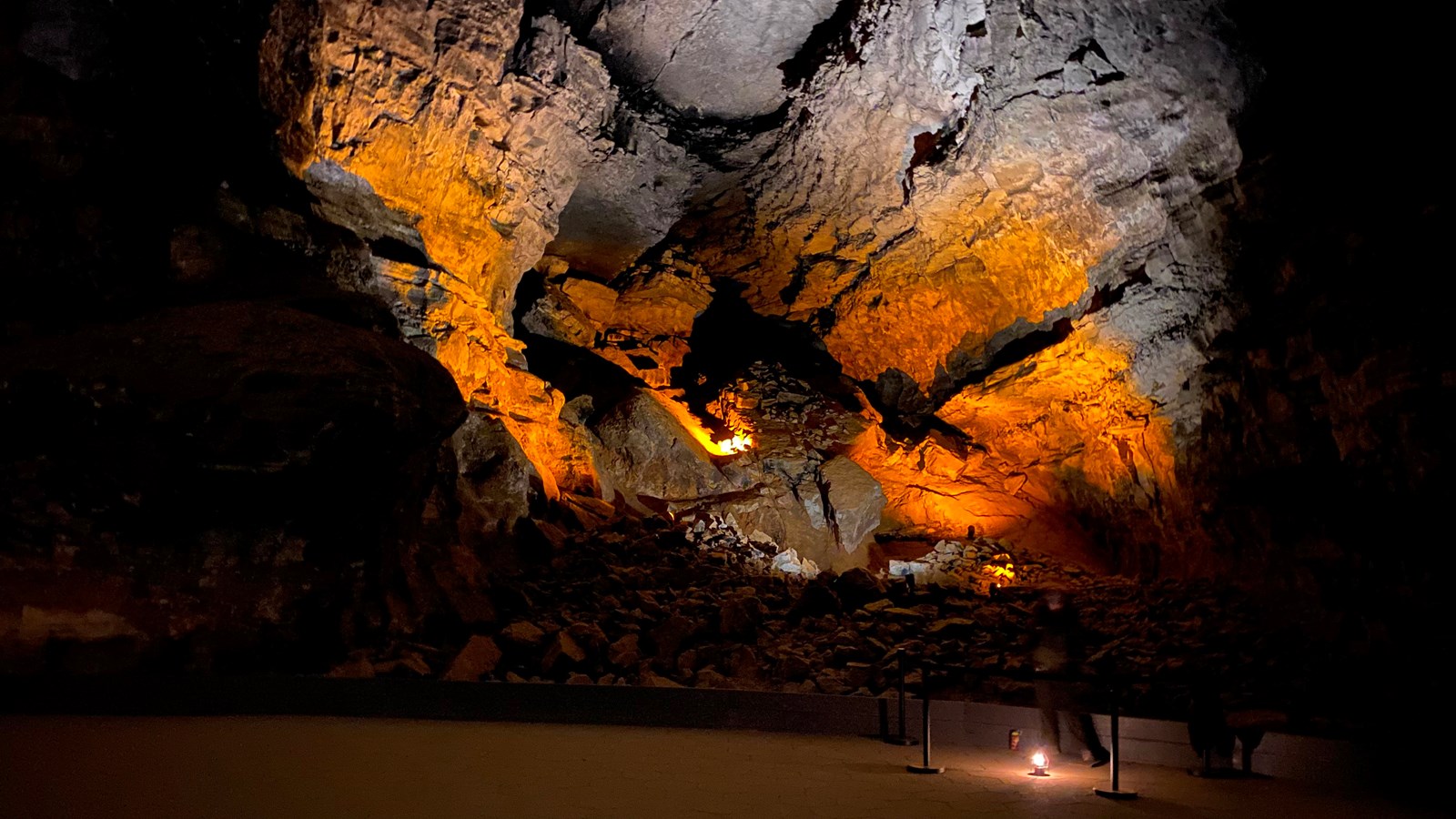 Towering cave walls lit up from below. A wide open paved trail is in the center of the room. 