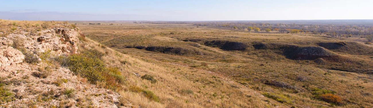 A rocky bluff looks out on a flat plain of sparse vegetation.