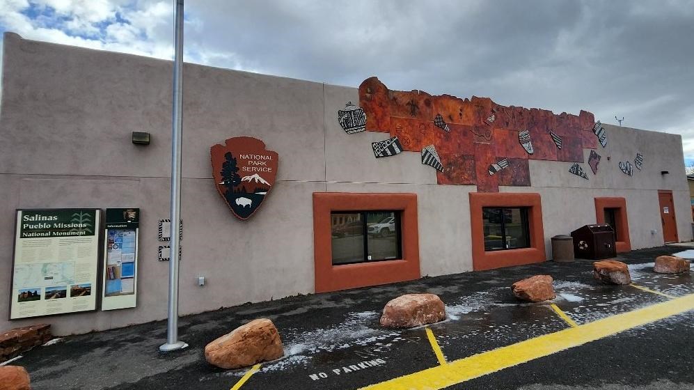 A tan building with a National Park Service arrowhead and pueblo themed artwork on the front face.