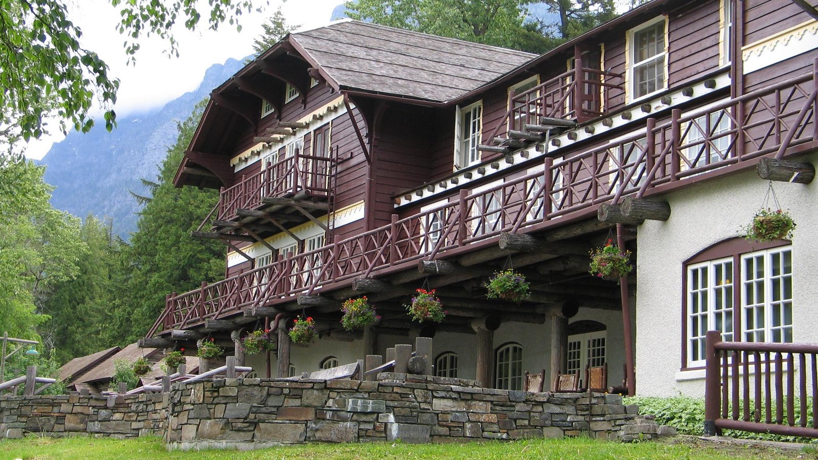 A rustic three-story lodge with dark brown wood and white stone decorated with hanging plants.