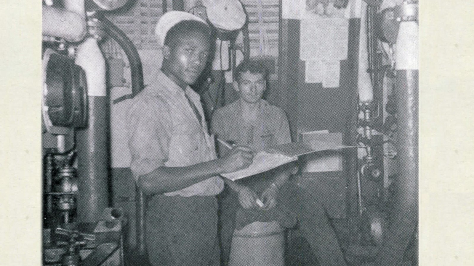 Two crew members taking readings of equipment in the Fire Room of a destroyer.
