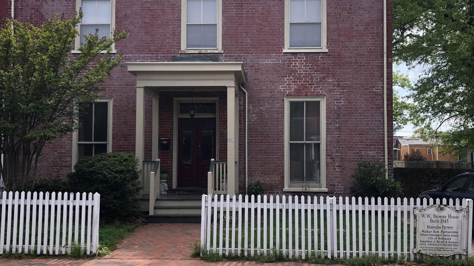 A two-story red brick home with a white picket fence surrounding the home