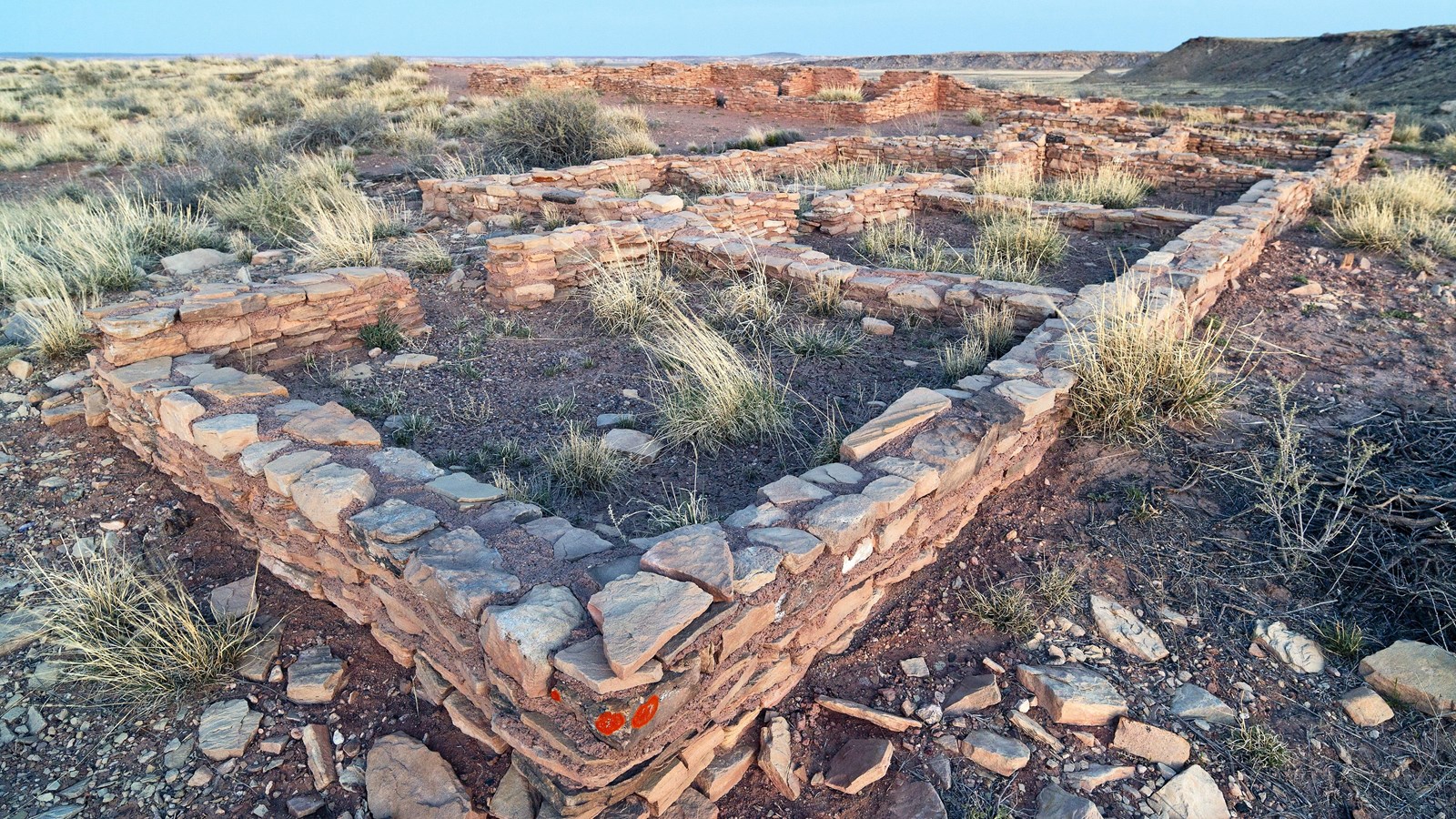 Remnants of archeological walls with a mesa beyond under a twilight sky.