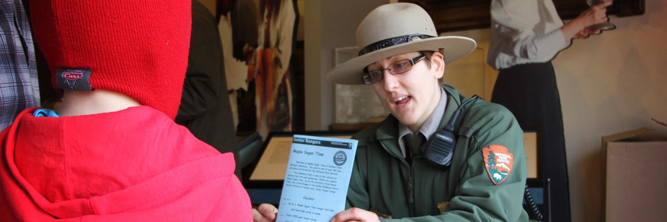 Ranger talks to child while holding a Junior Ranger booklet