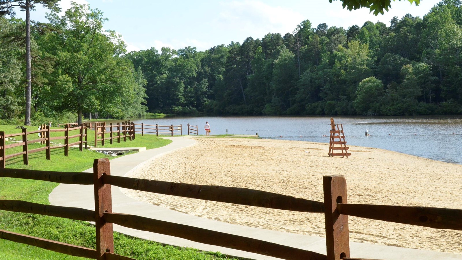 Image showing a small beach front on a lake. There is a brown fence along the perimeter.