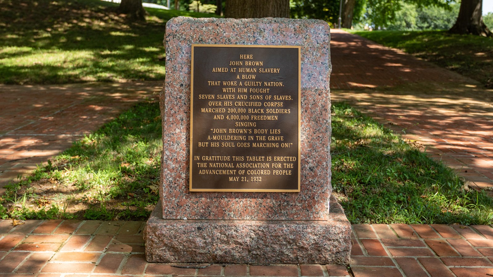 A brown plaque with gold lining and lettering is placed on a granite memorial. 
